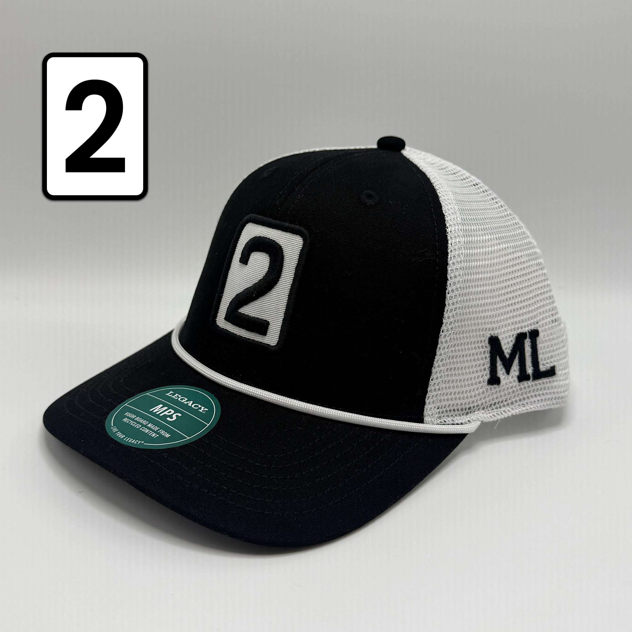 A black and white trucker cap with a black visor, black front panel with a white-bordered number 2 patch, white mesh back, and black 'ML' embroidery on the side. A white square with a black number 2 is shown in the top-left corner.
