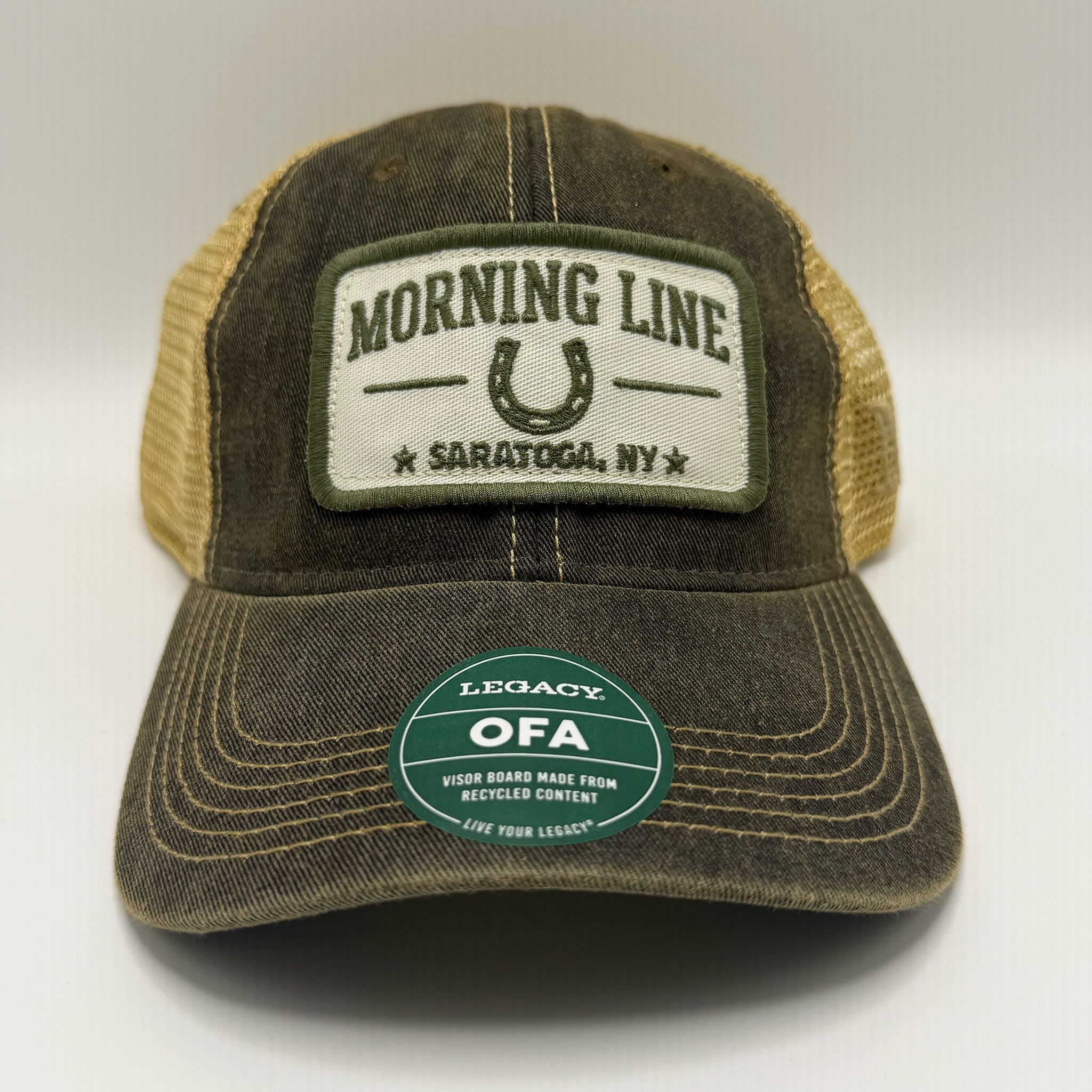 A distressed trucker hat in washed olive green and tan mesh, featuring a front patch that reads 'MORNING LINE SARATOGA, NY' with a horseshoe graphic, and a green circular 'Legacy OFA' sticker on the brim.